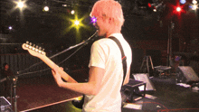 a man with pink hair is playing a guitar on a stage with a microphone