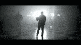 a man is standing in a dark room with a light behind him