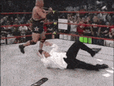 a man in a suit is laying on the ground in a wrestling ring while a wrestler runs towards him