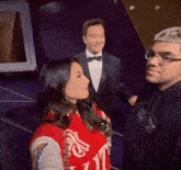 a man in a tuxedo and bow tie stands next to a woman wearing a red sweater that says t.j.