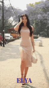 a woman in a white dress is walking down a sidewalk with elya written on the bottom right