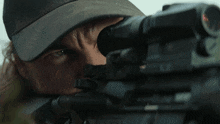 a man wearing a hat is aiming a rifle with a scope on it