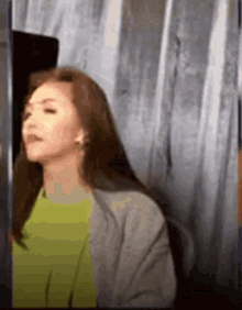 a woman in a green shirt and a gray jacket is standing in front of a glass wall .