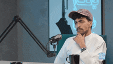 a man wearing a hat is sitting in front of a microphone with arabic writing on the bottom