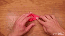 a person is holding a red origami object on a wooden table