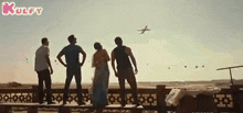a group of people standing on a balcony watching a plane take off .