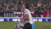 a female soccer player stands on the field in front of a banner that says " thank you men "