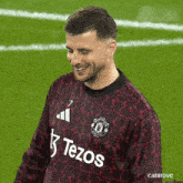 a man wearing a tezos jersey smiles on a field