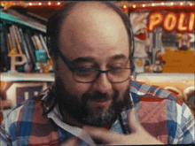 a man wearing glasses and a plaid shirt is standing in front of a neon sign that says poli
