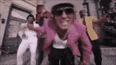 a man wearing a pink jacket and sunglasses is dancing with two other men