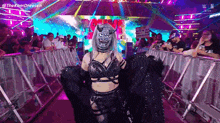 a woman in a mask is walking through a ring at a wrestling match .