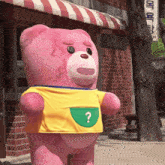 a pink teddy bear wearing a yellow shirt with a green question mark on it