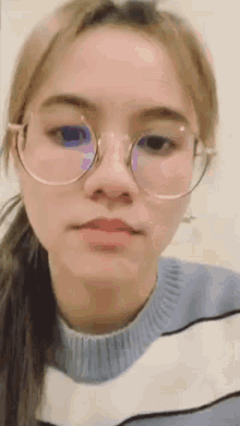 a young woman wearing glasses and a blue and white sweater is looking at the camera .