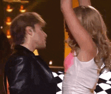 a woman in a white tank top is dancing with a man in a black jacket .