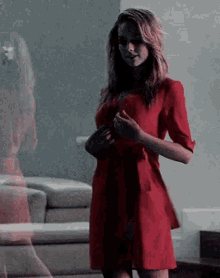 a woman is standing in front of a mirror wearing a red dress .