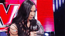a woman is holding a microphone in front of a red wall with a w logo on it .