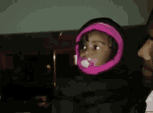 a baby with a pacifier in her mouth is wearing a pink hooded jacket .
