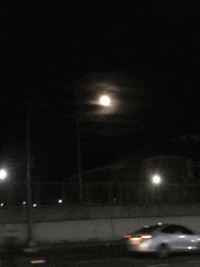 a car is driving down a street at night with a full moon behind it