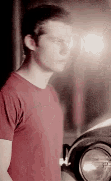 a young man in a red shirt is standing next to a car