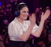 a woman wearing headphones applauds in front of a crowd of people
