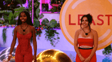 two women in red dresses stand in front of a sign that says least