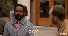a man in a sweater and tie says " okay " to another man