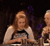 a woman wearing a shirt that says one day we 'll all be skeletons sits at a table with a man