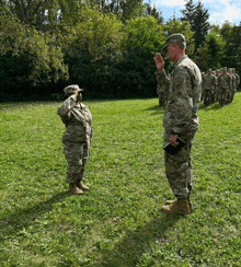 a man in a camouflage uniform salutes a woman in a military uniform