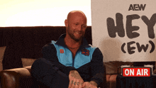 a man sits on a couch in front of a sign that says hey