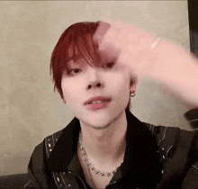 a young man with red hair is wearing a black jacket and a silver necklace .