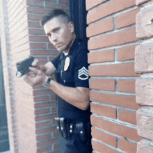 a police officer holds a gun while leaning on a brick wall