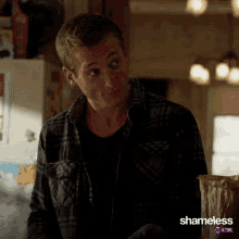 a man in a plaid shirt is standing in front of a shameless sign