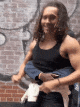 a man in a black tank top is carrying another man on his shoulders in front of a brick wall .