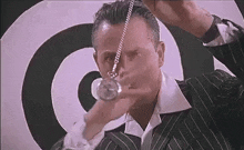 a man in a suit is holding a pocket watch in front of a hypnotic spiral .