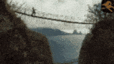 a person is walking across a rope bridge between two mountains