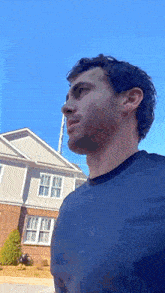 a man in a blue shirt is standing in front of a brick house