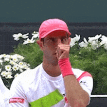 a man wearing a pink hat and a white shirt with a green stripe on the sleeve is covering his mouth
