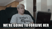 a man is sitting in front of a laptop with the words " we 're going to forgive her " on the screen