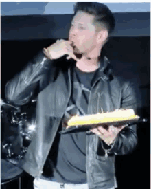a man in a leather jacket is holding a plate of cake