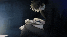 a man in a black shirt sits in a dark room looking at a piece of paper