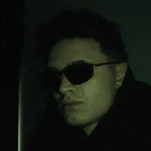 a man wearing sunglasses looks at the camera with a serious look on his face