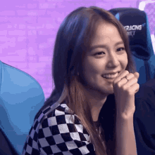 a woman in a black and white checkered shirt is smiling in front of a racing chair