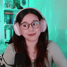 a woman wearing pink headphones and glasses looks at the camera