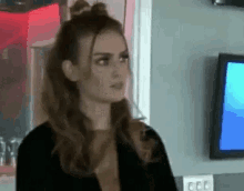 a woman is standing in front of a television in a room and looking at the camera .