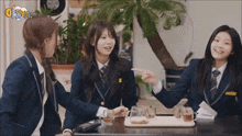 three girls in school uniforms are sitting at a table with a tray of drinks and a sign that says " open "