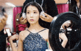 a woman in a blue dress is getting her hair done by a person wearing headphones