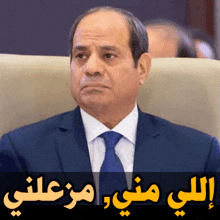 a man in a suit and tie sits in a chair with arabic writing below him