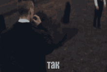 a man in a suit is smoking a cigarette and the word tak is on the bottom of the image .
