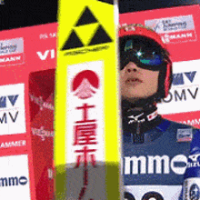 a man wearing a helmet and goggles is holding a pair of skis with chinese writing on them