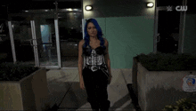 a woman with blue hair is walking in front of a building with a sign that says cw on it